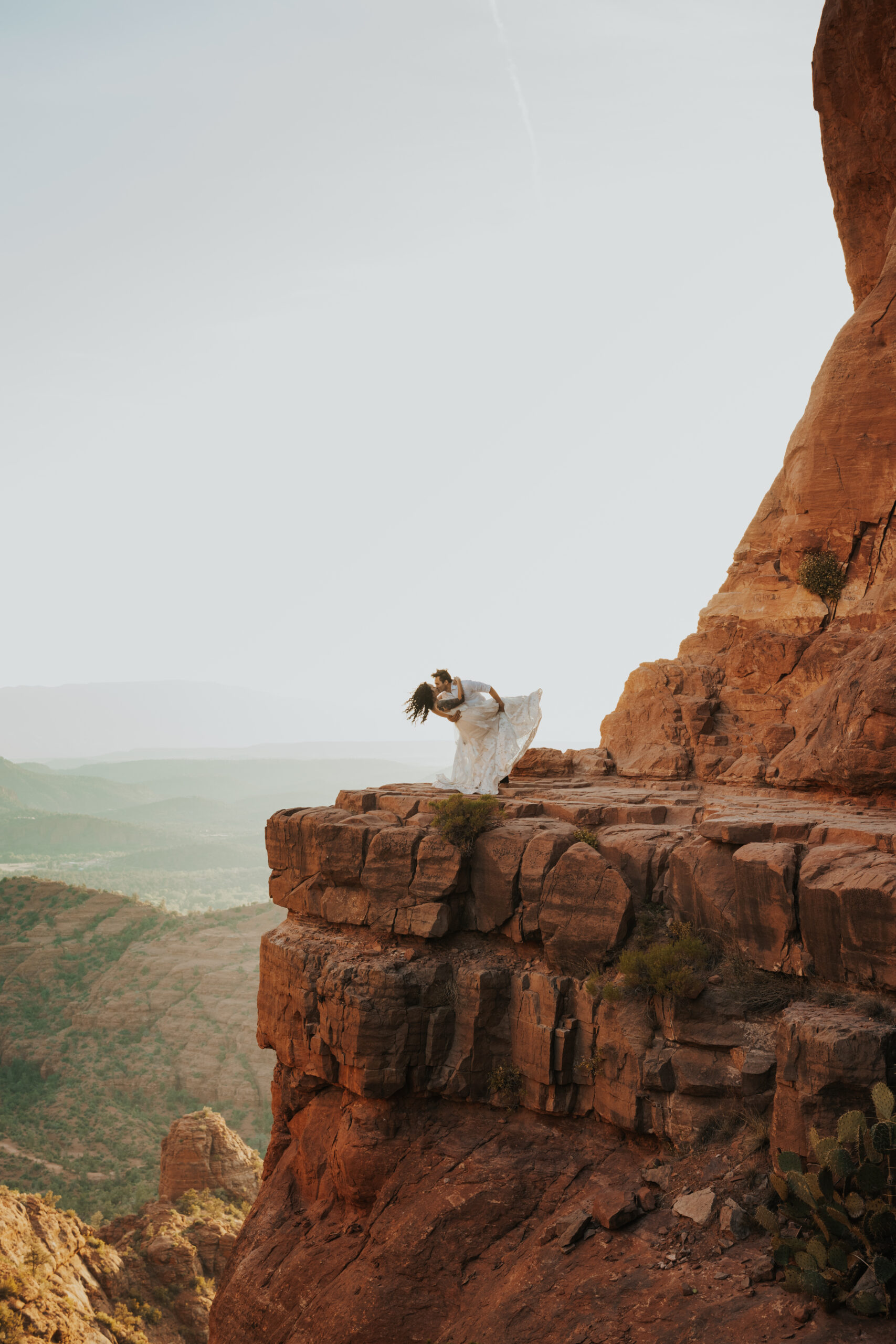 man dips woman in wedding dress on the ledge of cathedral rock