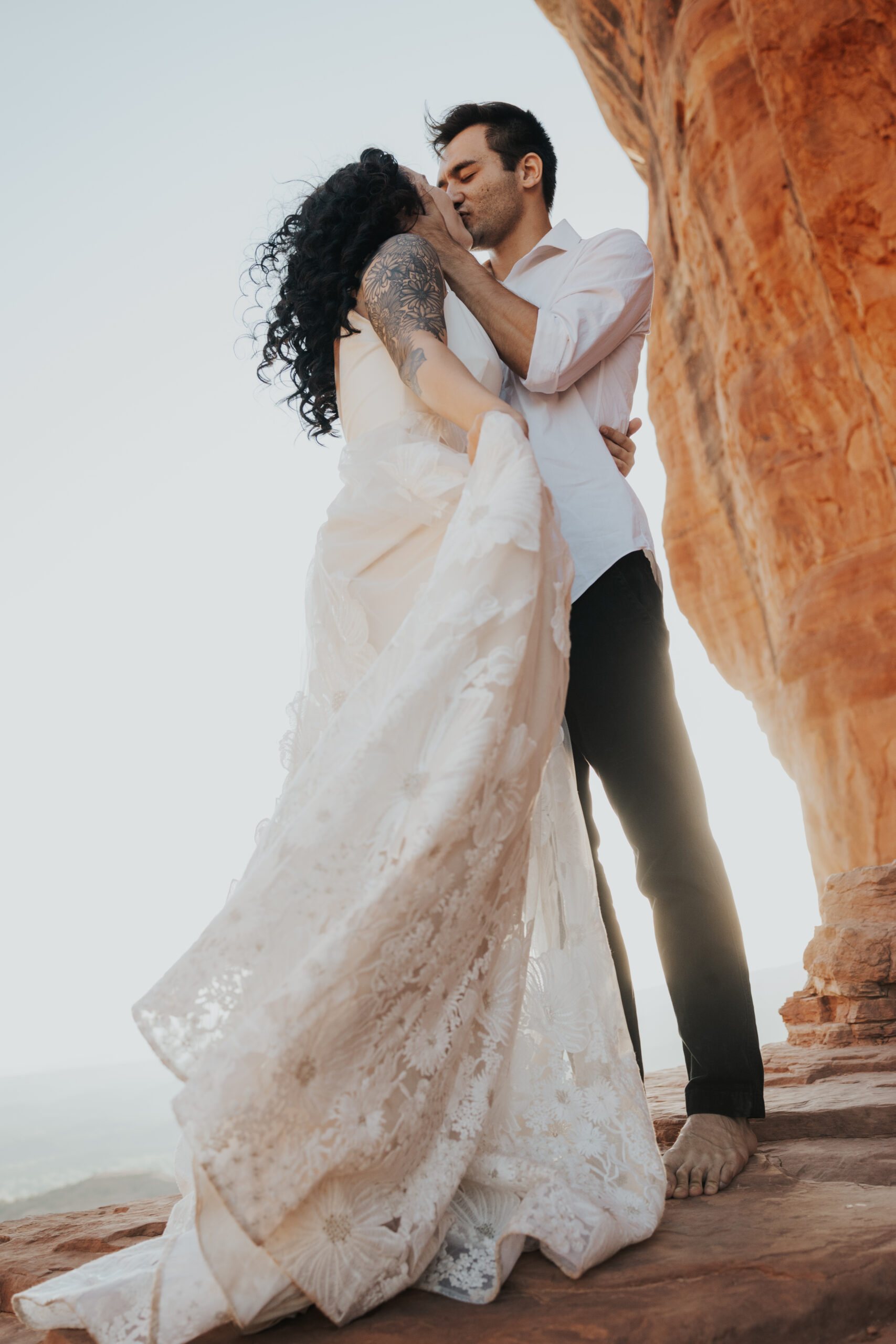 a couple embraces beautiful flowing wedding dress low angle shot on ledge of cathedral rock