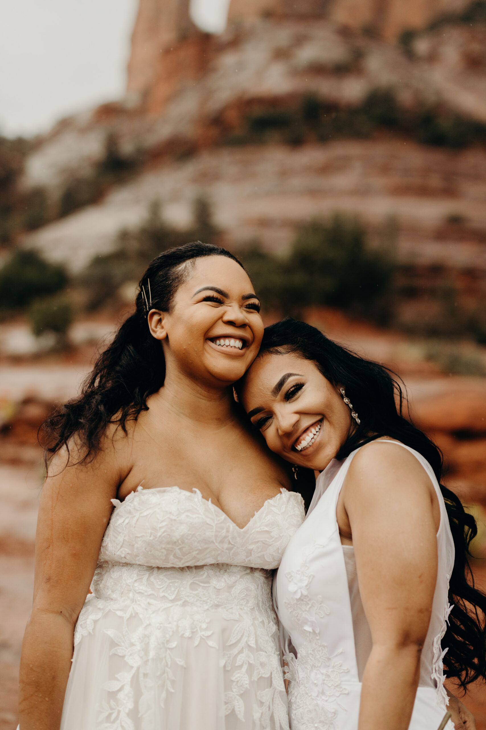 two woman in wedding dresses on cathedral rock smiling