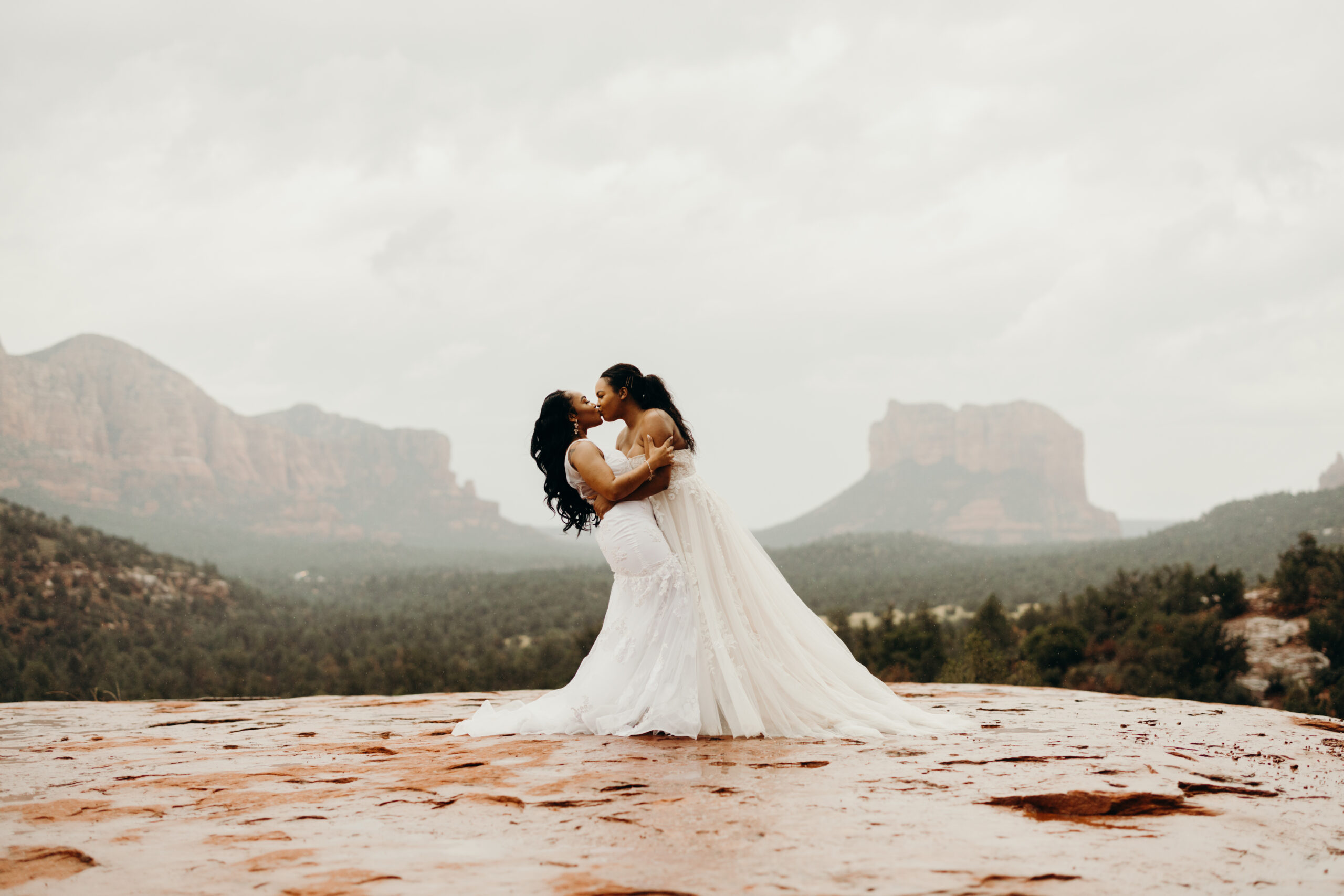 two woman kissing in wedding dresses beautiful rainy scenic view on the base of cathedral rock